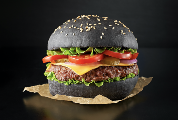 A gourmet burger served on a striking jet-black bun colored with BioconColors vegetable carbon natural colorant, showing a soft texture and intense color stability.
